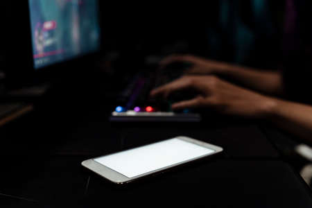Hands of gamer playing game, typing on keyboard. Empty screen on smartphone putting close to keyboard.の写真素材