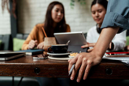 Two young ladies working together on tablet while her boss is watching. Modern technologies in daily...