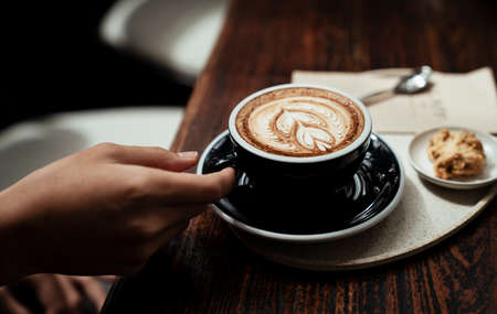 A customer holding a cup of coffee lattee on wooden table.