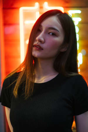 Fashion portrait - Beautiful hipster asian young woman in black shirt over neon light background....