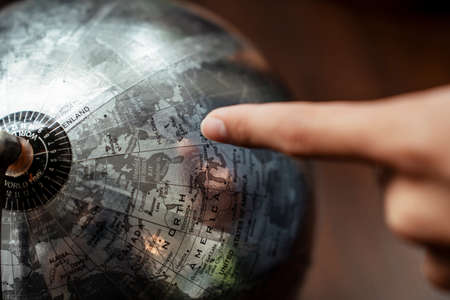 A finger pointing at the country on the world globe map made of metal material.の写真素材