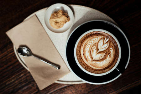 Coffee latte art in a luxury cup serve with a piece of cookie on a plate.