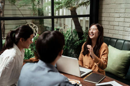Asian woman laughing in the middle of casual meeting at modern cafe.の写真素材