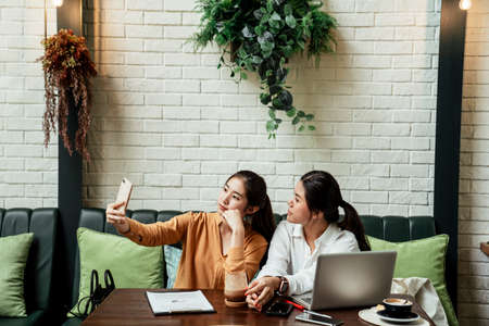 Two asian women taking selfie with smartphone on the couch in cafe.の写真素材