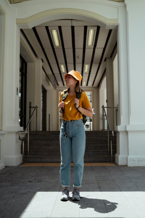 Yellow backpacker woman with green backpack standing in the light in front of the entrance of white...