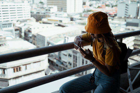 Backpacker girl standing at the handrail watching the photo in her smartphone.の写真素材