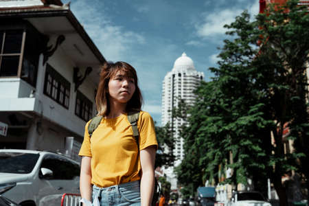 Yellow backpacker woman with green backpack standing in the city with temple, tree and high building as a background.の写真素材
