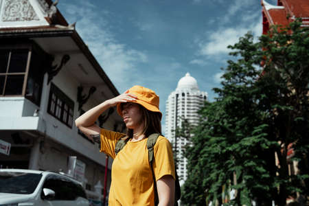 Backpacker girl in yellow t-shirt grab her hat while travelling at the temple in a city.の写真素材