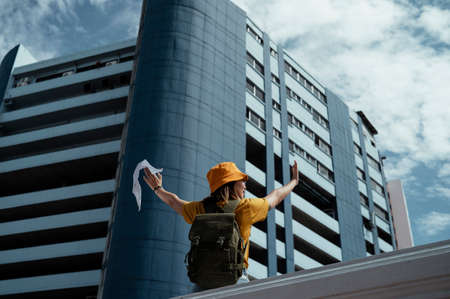 Yellow backpacker woman with green backpack raise her hands to the sky with happiness.の写真素材