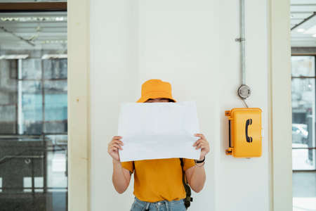 Yellow backpacker woman with green backpack standing at the yellow payphone and show the white...