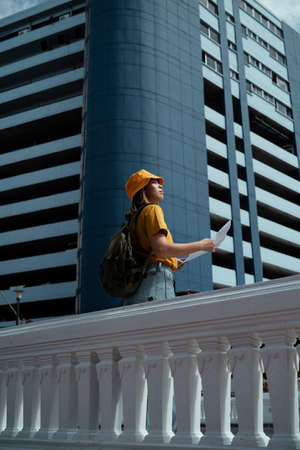 Long shot of backpacker girl looking at the map to locate herself while she travel in the big city.の写真素材