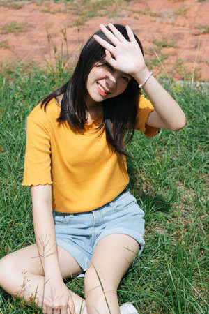 Black long hair girl sitting on the grass field, raise her hand guars against the sunlight.の写真素材