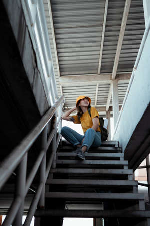 Yellow backpacker woman with green backpack sitting at the top of stair and enjoy the fresh air.の写真素材