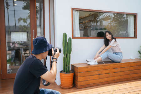 Male photographer take a photo of teenage model girl in front of the cafe with cactus and wooden floor.の写真素材