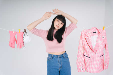 Beautiful asian thai long dark hair woman in pink shirt hanging herself on cloth rack with wet clothes over white background.の写真素材