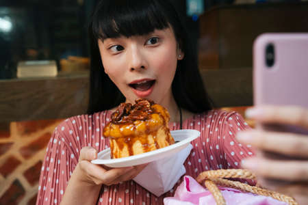 Beautiful asian thai long dark hair woman taking selfie with bread cake at cafe bakery shop.の写真素材