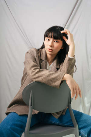 Beautiful asian thai long dark hair woman in jacket suit and jeans pants sit on chair. Fashion portrait.の写真素材