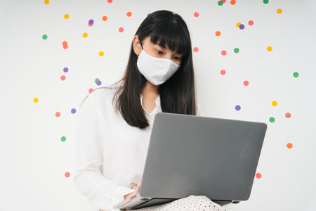 Beautiful asian thai long dark hair woman wearing white surgical mask using laptop isolate over white party background. Work from home concept. Business woman working with computer laptop.の写真素材