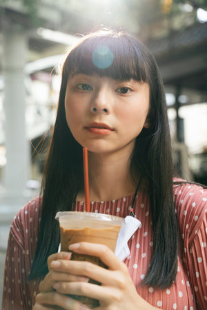 Beautiful asian thai long dark hair woman drinking ice cold coffee cup with straw outdoor on street.の写真素材