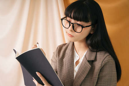 Beautiful businesswoman wearing eyeglasses and suit jacket looking a report on a book. Pretty nerd...