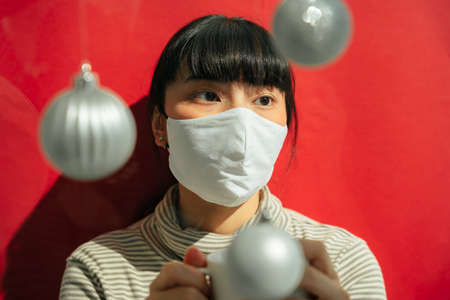 Fashion portrait - Beautiful asian thai long dark hair woman wearing surgical mask over red background. New normal fashion.の写真素材