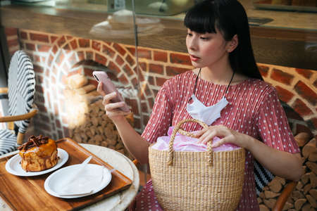 Beautiful asian thai long dark hair woman taking photo of bread cake before eating. Camera eat first concept.の写真素材
