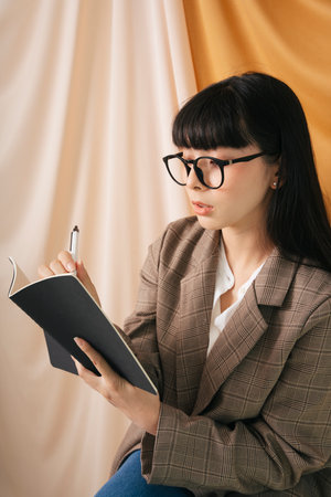 Thoughtful Beautiful asian thai long dark hair woman in jacket suit hold a book and pen. Fashion portrait.の写真素材