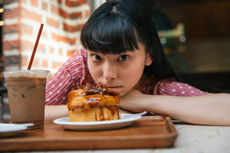 Beautiful asian thai long dark hair woman at bakery cafe shop with bread cake and ice coffee. Excited and amazed expression.の写真素材