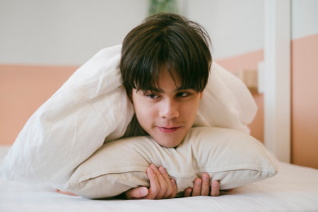 Introvert guy lie down on his stomach on the bed and hug the pillow, he's smile while thinking about good memory.の写真素材