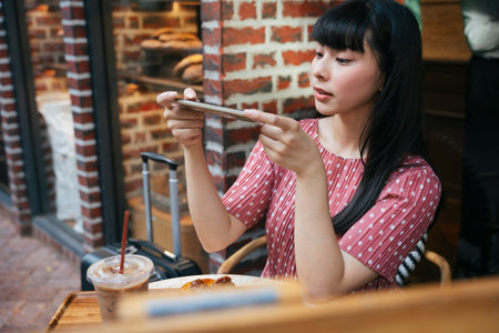 Beautiful asian thai long dark hair woman taking picture of bread cake with smartphone at cafe. Camera eat first.の写真素材