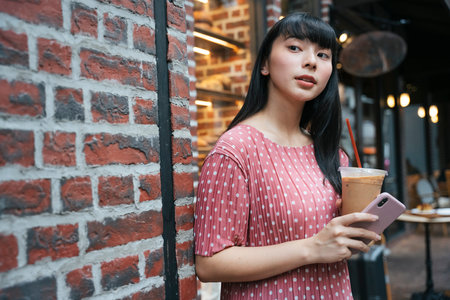 Beautiful asian thai long dark hair woman with ice coffee and smartphone in Bangkok street.の写真素材