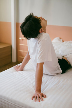 Black hair guy sit on white bed, lean back on his arms and look at the ceiling.の写真素材