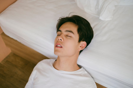 Black hair guy sit on the floor next to the bed, prop his head on the bed and close his eyes, it's a weird sleeping posture.の写真素材