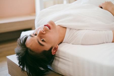 Black hair guy lie down on the bed, let his head drop from the bed.の写真素材