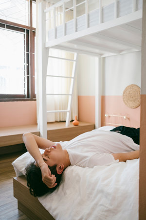 Introvert guy lie down on the bed and put his arm on his forehead like he's thinking about his problem.の写真素材