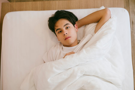 Black hair guy lie down on bed and put his head on his hand look at the camera without facial expression.の写真素材