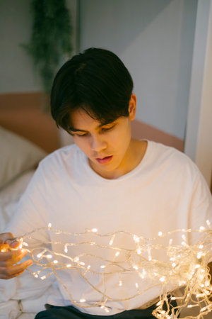 Cute guy in white t-shirt play the light in his hands. He try to make the decorative lights to not be messy.の写真素材