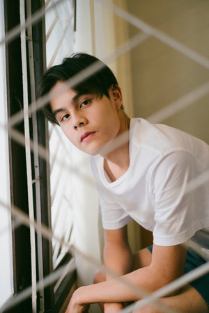 The guy in white t-shirt sitting near by the window, looking outside with empty mind.の写真素材