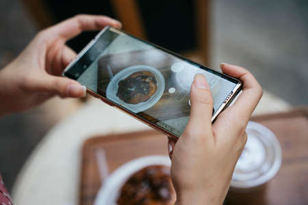 Close up - Woman hand taking photo with smartphone in bakery shop. Camera eat first.の写真素材