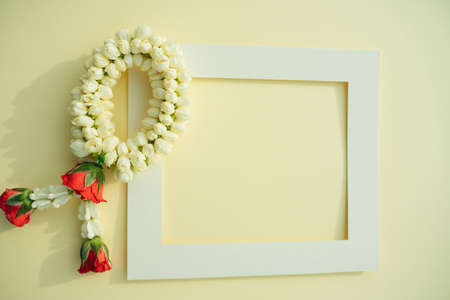 Thai Flower Garland with jasmine & roses with mock up white frame over bright yellow background. Top view.の写真素材