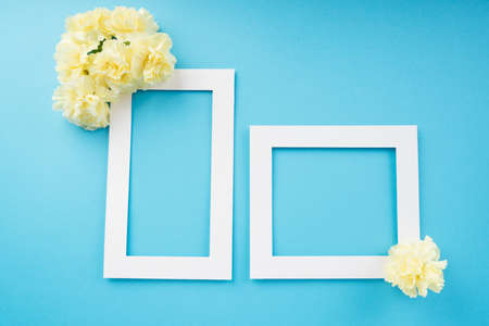 Mock up white frame with yellow flower over bright blue background. Top view. Copy space.の写真素材