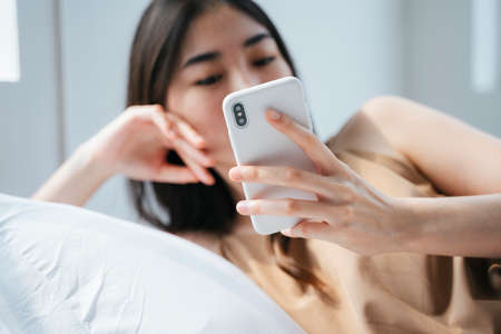 Cropped image of smartphone in girl's hand while she bend down on the pillow and access to her social media account.の写真素材