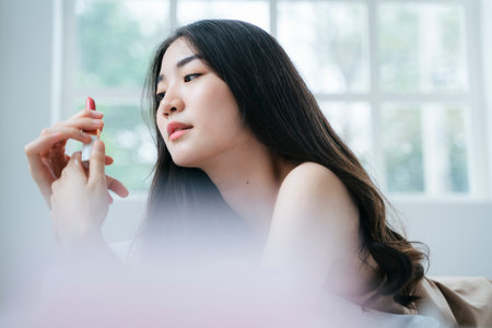 Wavy long hair woman lie down on stomach on the bed in the morning and holding the lipstick then rotates it.の写真素材