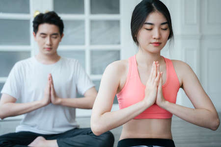 Long hair woman in old rose color sport bra getting home yoga with male personal trainer, sitting on the floor in the prayer position.の写真素材