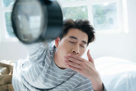 A man sleep on the white bed, the alarm clock wake him up in the morning.の写真素材