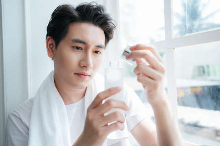 A man in white t-shirt hold the bottle of moisturizer lotion after take a shower.の写真素材