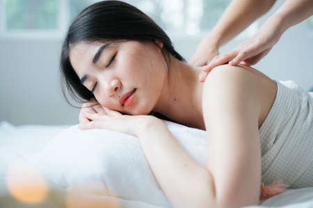 Long hair girl in white towel lie down on the white bed whle getting relax with Thai massage in the spa.の写真素材