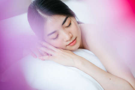 Long hair girl in white towel lie down on the white bed whle getting relax with Thai massage in the spa.の写真素材