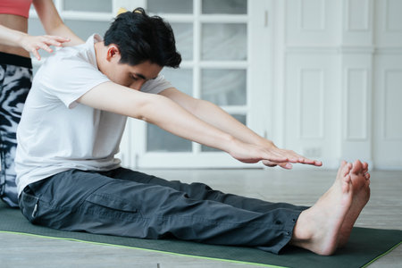 A man getting home yoga with female personal trainer in old rose color sport bra.の写真素材