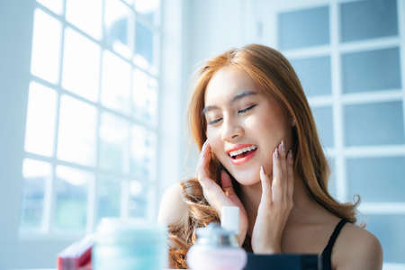 Wavy blond hair girl sitting in front of lots of cosmetics and skincare for her healthy skin.
